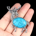 Silver elk brooch with large sky blue oval stone held in hand against black background - Blue Turquoise (Synthetic)