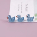 Close-up of three mini blue resin ducks with glitter finish on a soft purple base - Blue