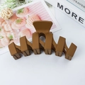 Brown matte wave-shaped claw clip with geometric cutout design on a clean desk - Yellow Coffee