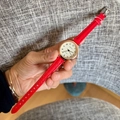 Close-up of a women's quartz watch with red leather strap and gold-tone case held in hand - Red Ribbon