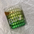 Close-up of green gradient spiral hair ties in a transparent box on textured paper - Green