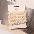 Close-up of four-piece beige satin scrunchie set on a white display card in soft lighting - Off-white