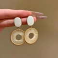 Detail of hand holding gold-tone round resin hoop earrings with woven texture - 6# Silver Earring Post-White (Woven Hollow Round)