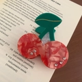 Rode gemarmerde kersenvormige haarklem met groene bladeren op een open boek - Kers (6cm)