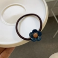 Dettaglio di elastico per capelli marrone con fiore blu e centro arancione in un vassoio bianco - Elastico per Capelli con Fiore Piccolo / Blu scuro