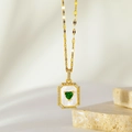 Detailed close-up of a gold heart pendant with green gemstone on a marble background - Green