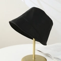Minimalist black bucket hat shown on a gold metal stand in a lifestyle home setting - Black