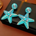 Detail van turquoise zeester oorbellen met fonkelende strassteentjes en witte parels - Zilveren oorknopje-Blauw