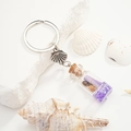 Close-up of glass bottle keychain with purple glitter, sea shells and paper scroll - Violet