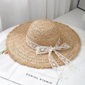 Top view of wide brim raffia sun hat featuring white lace embroidery and chic bow detail - White Lace