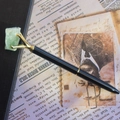 Macro detail of black metal ballpoint pen with gold claw holding a green crystal stone - Aventurine Jade