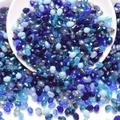 Detail of blue teardrop faceted glass beads scattered from a white ceramic bowl - Blue Series