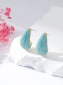 Macro shot of gold teardrop earrings with turquoise bead inlay on white stone - Turquoise
