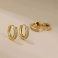 Orecchini a cerchio dorati con pavé di cristalli scintillanti su sfondo beige - Cerchi in zirconia a più file