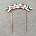 Detail of Merry Christmas cake topper featuring red lettering and green leaves with wooden sticks - Red Merry Christmas Banner
