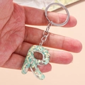 Detail of keychain with transparent resin letter R filled with green sparkling sequins - Letter R