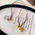 Macro view of matte gold gourd pendant with intricate woven rope knot on linen backdrop - Coffee Cord Style