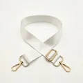 Detail view of adjustable white nylon bag strap with polished gold metal hardware and hooks - White