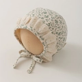 Dettaglio della cuffietta floreale per neonati con pizzo e lacci su supporto di legno - 35-45cm (0-12 Mesi) / Verde