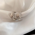 Macro view of silver teardrop cross C-shape earrings on white silk fabric background - Silver