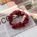Detail of wine red satin scrunchie showing soft fabric texture on newspaper background - Burgundy