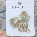 Détail d'une broche en forme de nœud doré avec perles blanches et strass étincelants - Style B244