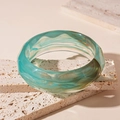 Close-up of green marble-patterned acrylic bangle resting on a travertine stone - Blue