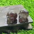 Two smokey quartz crystal skulls carved from natural stone on a wet wooden base - Strawberry Quartz