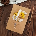 Handmade kraft paper greeting card with yellow dried flowers on dark wood surface - Miracle