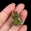 Miniature hand-carved unakite crystal wolf figurine held between fingertips - Unakite