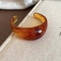 Detalle del brazalete de resina ámbar mostrando textura jaspeada sobre fondo de libro - Marrón