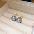 Detailansicht grauer Perlenohrringe mit Goldhaken in einer beigen Samt-Schmuckschatulle - 13mm Graue Perle Goldener Ohrhaken