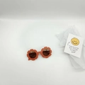 Close-up of orange flower-shaped kids sunglasses on a white background with a smiley card - Orange