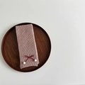Detail of pink knitted scarf with red ribbon bow and white pom-poms on wooden tray - Khaki