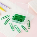 Green coated metal paperclips in a clear storage box on a pastel workspace - Green