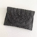 Close-up of black woven raffia envelope clutch bag showing detailed straw texture - Black