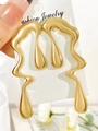 Close-up of golden liquid metal earrings with irregular drop design on jewelry card - KC Gold