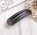 Matte black oval hair clip with hollow detail on white textured background - Black