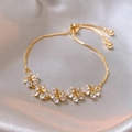 Close-up of gold-plated bracelet with zircon flower charms on white satin background - Gold