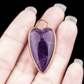 Amethyst heart pendant with gold rim held against black background for jewelry diy - Amethyst