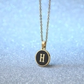 Golden round pendant necklace with black enamel inlay and letter H on blue bokeh - Letter H