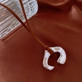 Foto macro de un colgante plateado irregular en forma de C con cordón de cuero marrón - Colgante de Metal Irregular en Forma de C / Collar-Café