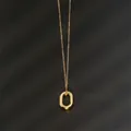 Flat lay of minimalist gold oval pendant necklace on a textured black background - Round