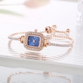 Detail shot of a rose gold square watch with blue dial and crystals on textured surface - Blue