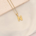 Golden letter N pendant necklace with textured finish on a white ceramic plate - Letter N