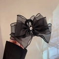 Détail d'une pince à cheveux avec nœud en maille noire et centre en strass étincelant - Dentelle Double Face Noire Avec Strass