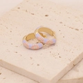 Macro shot of purple enamel daisy hoop earrings with gold edges on stone background - Purple