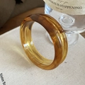 Detailed view of amber tortoise shell acrylic resin bangle on vintage beige linen books - Coffee Thick Cylindrical Style