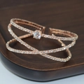 Detail of luxury rose gold criss-cross bangle with sparkling rhinestones on wood display - Rose Gold