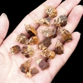 Natural tiger eye raw stone pendants with gold plated loops held in a hand - Tiger's Eye